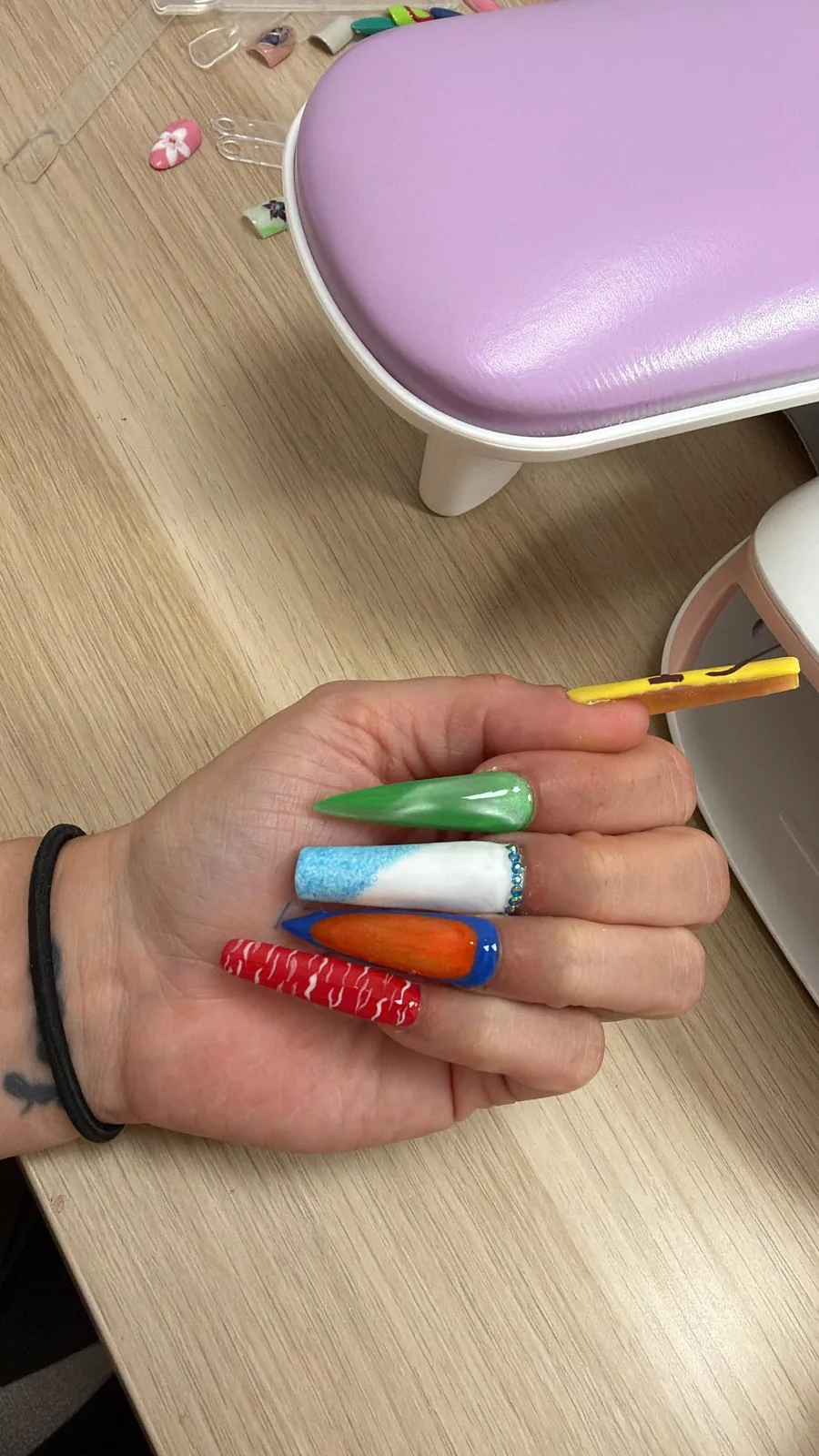 Kleurrijke lange nageltips naast een lila lamp